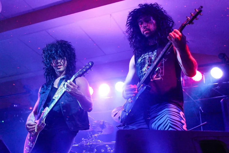Two guitarists back to back in purple light