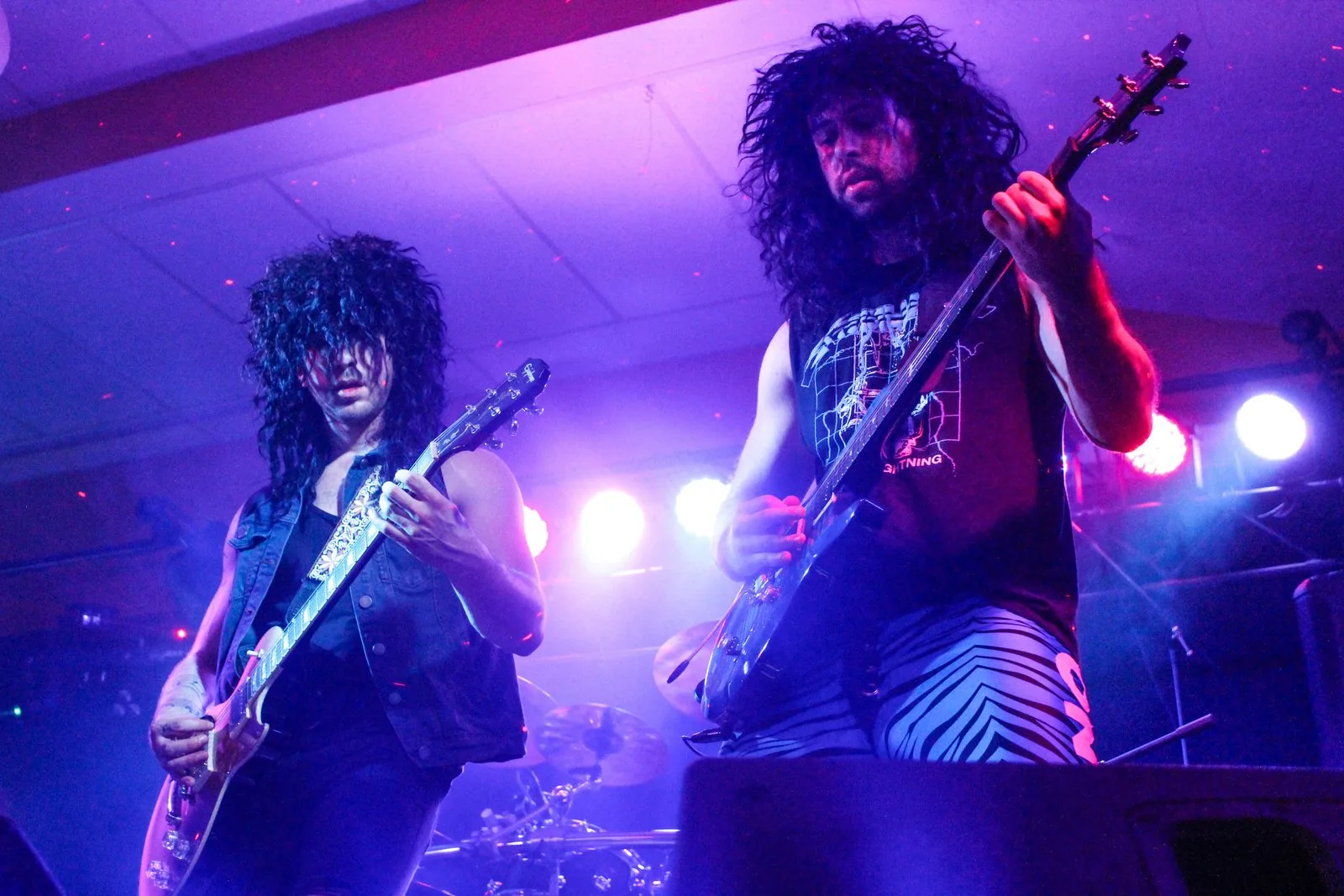 Two guitarists back to back in purple light